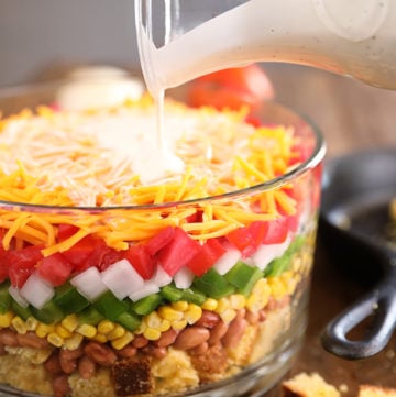 Layered Cornbread Salad in clear glass bowl - buttermilk ranch being poured over the top