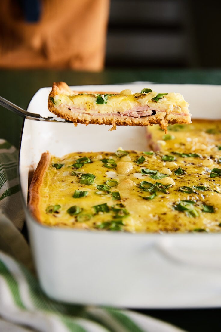 Slice of Ham and swiss breakfast casserole in a white dish.
