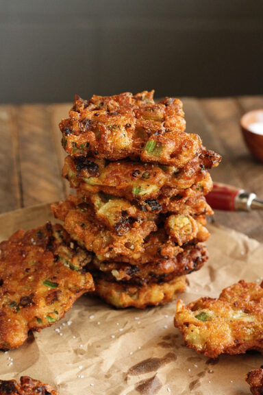 Okra and Green Tomato Fritters stacked on brown parchment paper.